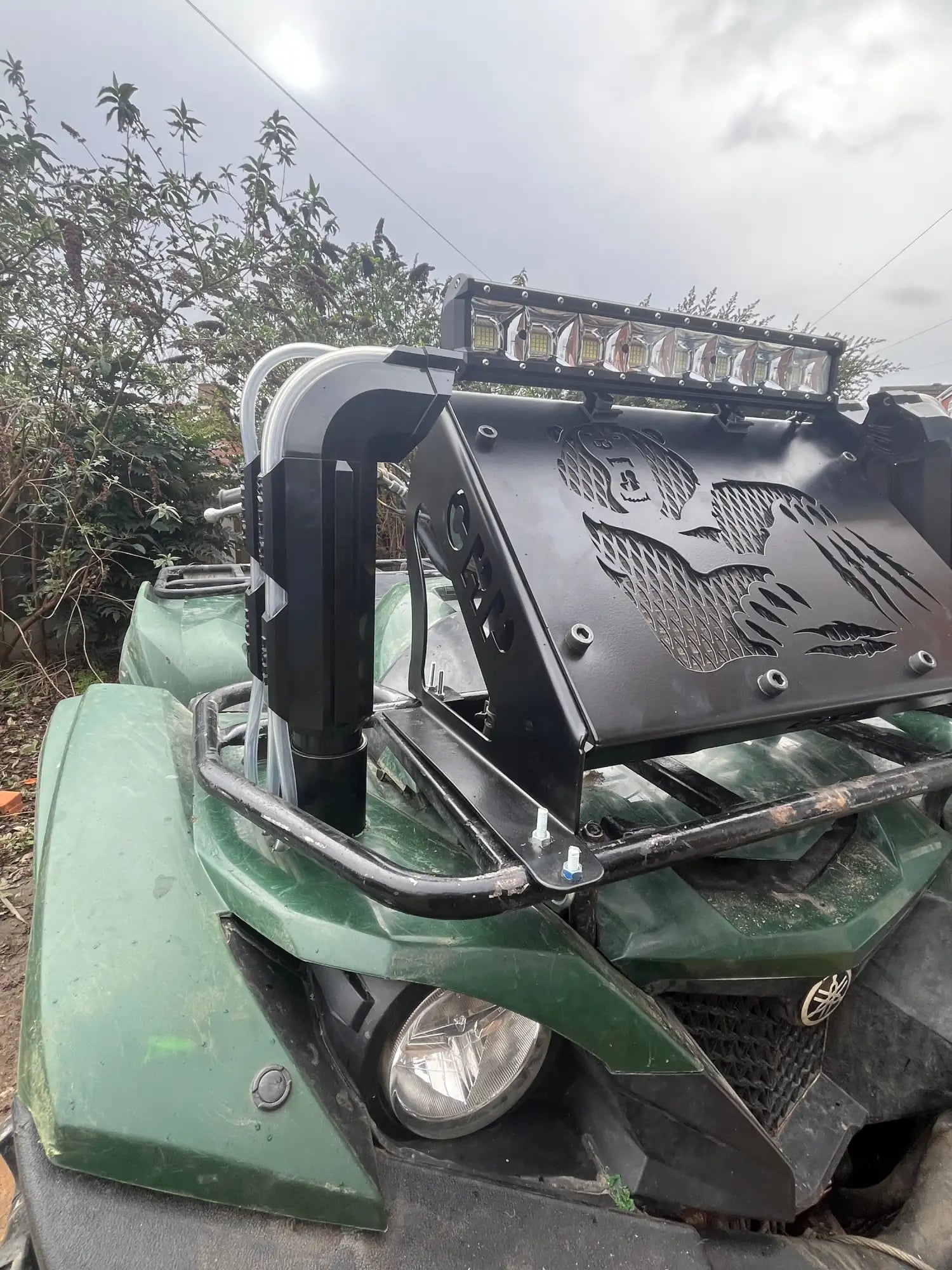 Close-up of a green ATV with a black metal attachment on a cloudy day.