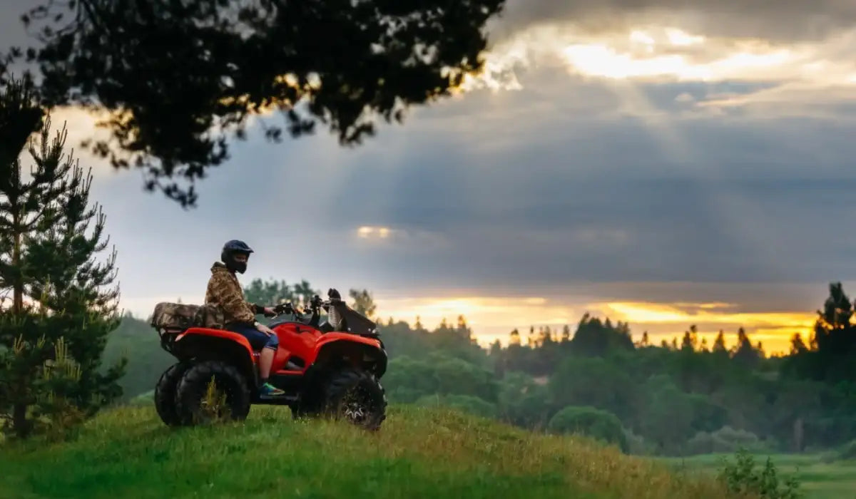 Person riding an ATV on a grassy hill with a scenic sunset in the background